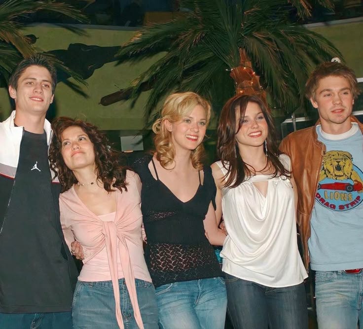 This may contain: a group of young people standing next to each other in front of a palm tree