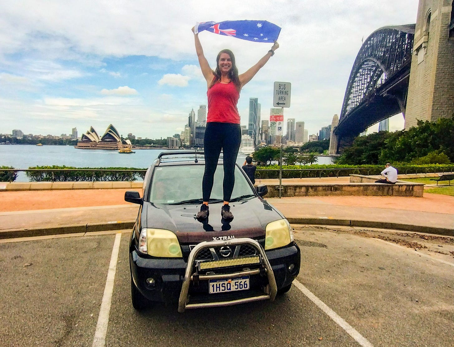 A person stands on the hood of a Nissan X-Trail SUV holding an Australian flag aloft, with the Sydney Opera House, Harbour Bridge, and city skyline visible in the background. A person stands on the hood of a Nissan X-Trail SUV holding an Australian flag aloft, with the Sydney Opera House, Harbour Bridge, and city skyline visible in the background.