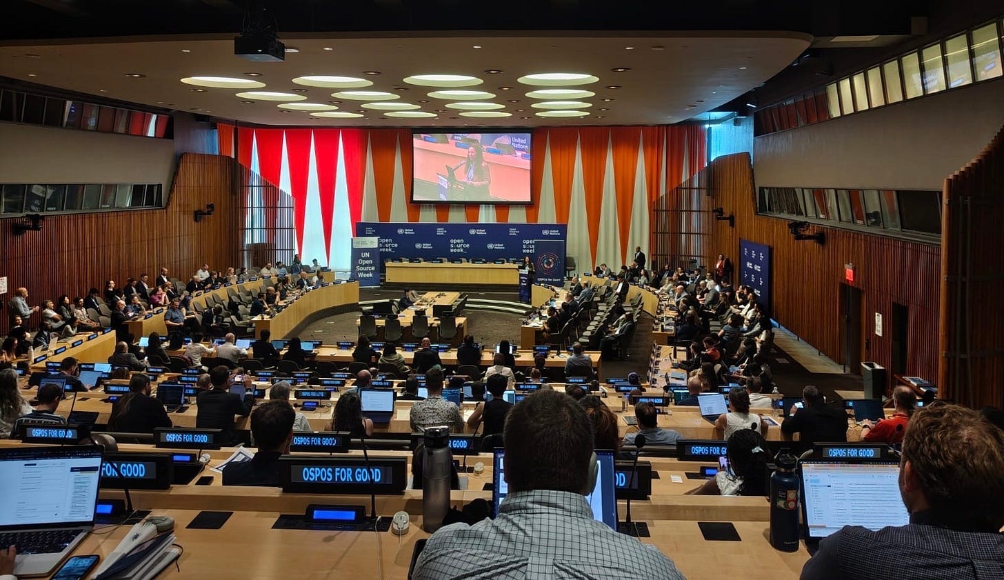 The ECOSOC Chamber at United Nations Headquarters during UN Open Source Week, filled with attendees at tiered desks with 'OSPOs for Good' placards, a speaker on the large screen at the front of the room. The ECOSOC Chamber at United Nations Headquarters during UN Open Source Week, filled with attendees at tiered desks with 'OSPOs for Good' placards, a speaker on the large screen at the front of the room.