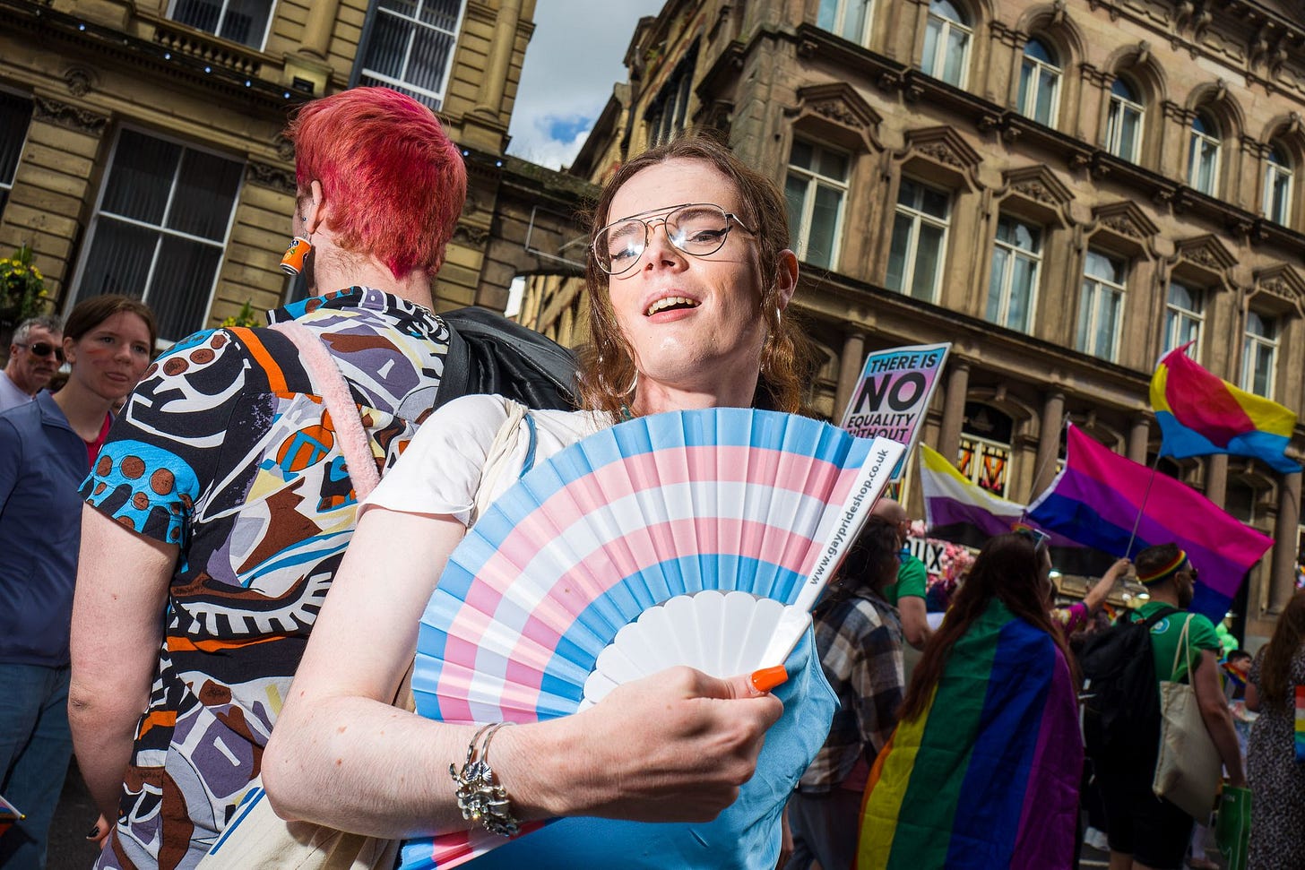 A person waves a trans flag themed fan during a march.