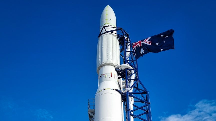 A white rocket, thinning as it reaches the nose, potining straight into a clear blue sky, with black ramps and an Australian fla