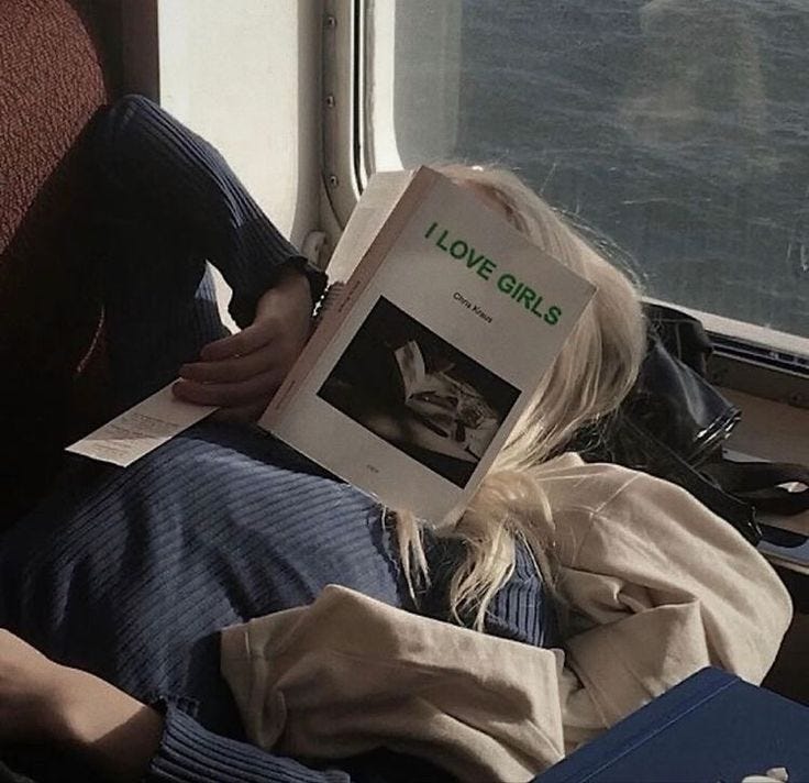 This may contain: a person laying on a train with a book in their hand and looking out the window