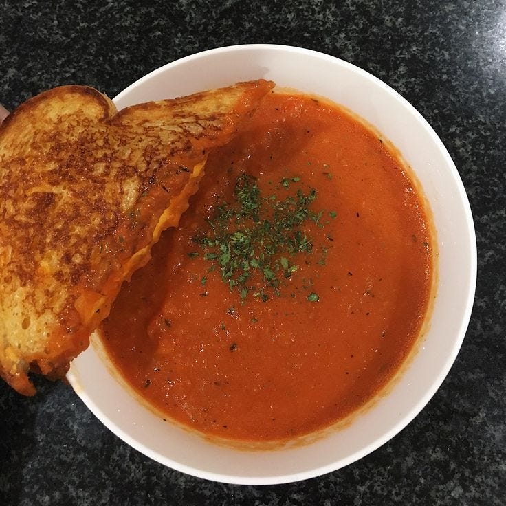 This may contain: a white plate topped with a grilled cheese and tomato soup