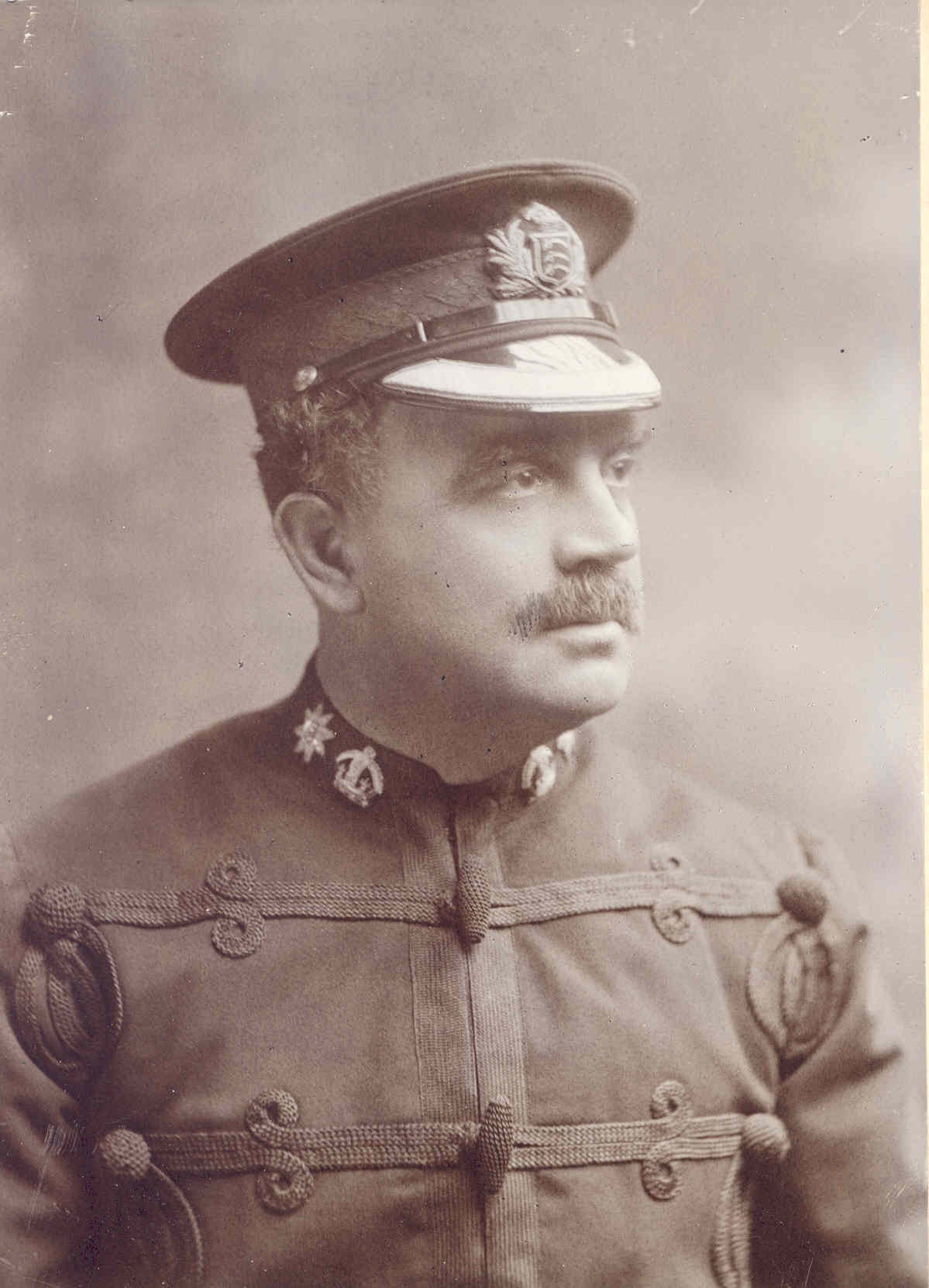 An officer wearing an early 1900s tunic and hat, featuring a merit star on the lapel.