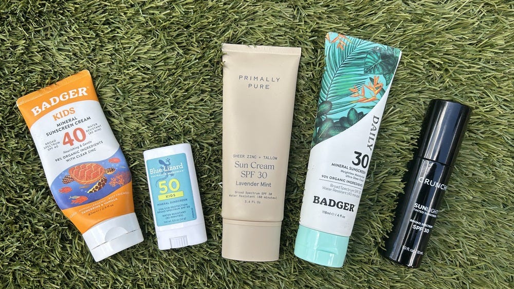 Five mineral sunscreens lined up on grass: Badger Kids 40, Blue Lizard Kids 50, Primally Pure Sun Cream SPF 30, Badger Daily 30, and Crunchi Sunlight tinted.