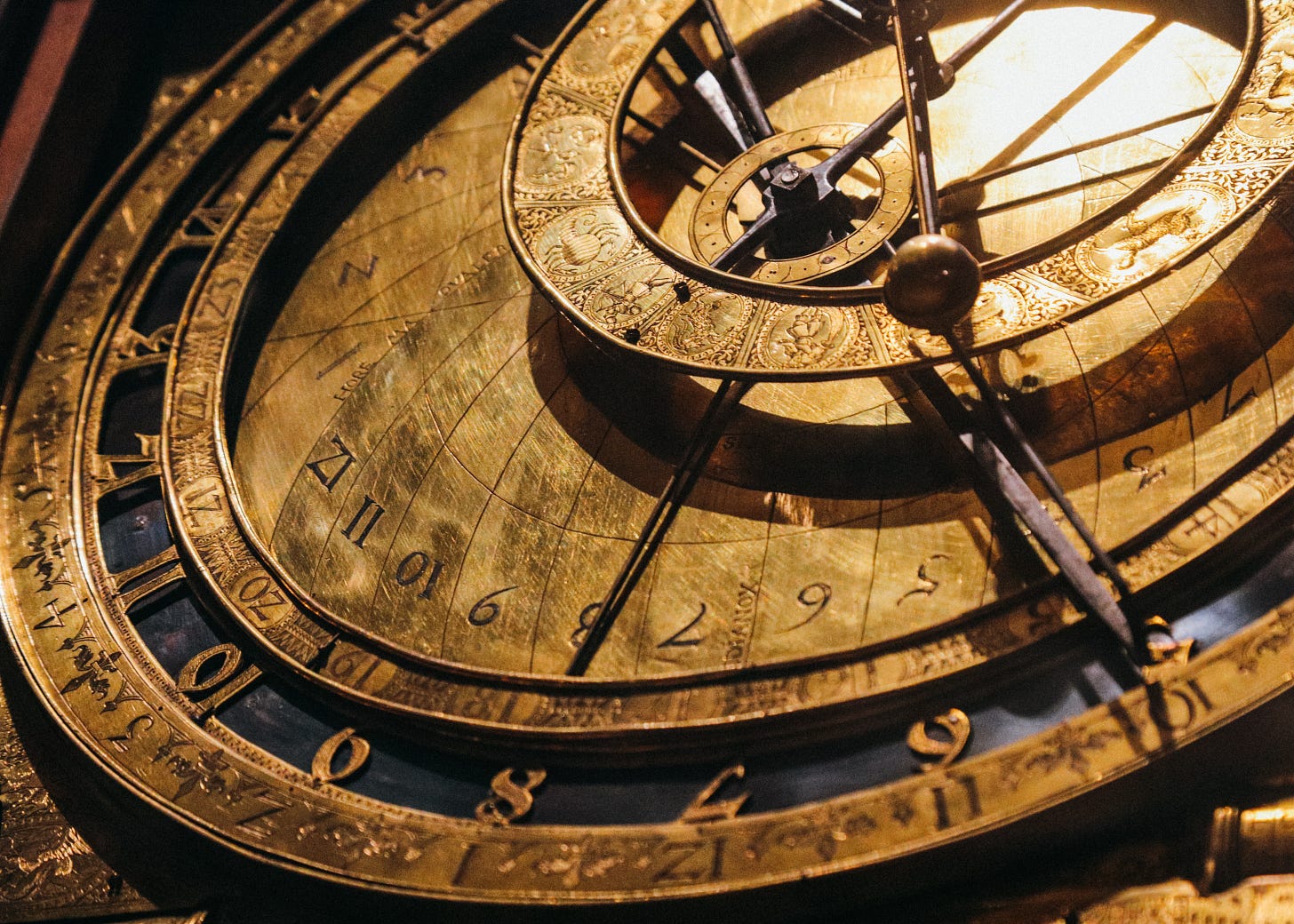A close-up photo of a complex brass clock face, including several offset rings showing time, zodiac, etc. A close-up photo of a complex brass clock face, including several offset rings showing time, zodiac, etc.