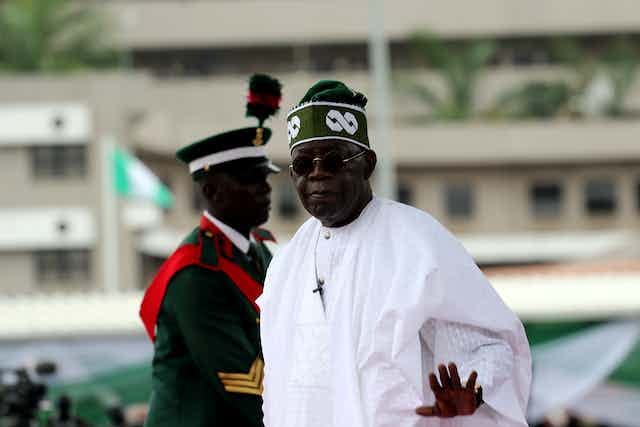 A man wearing white dress with traditional cap in front of a military officer in ceremonial uniform A man wearing white dress with traditional cap in front of a military officer in ceremonial uniform