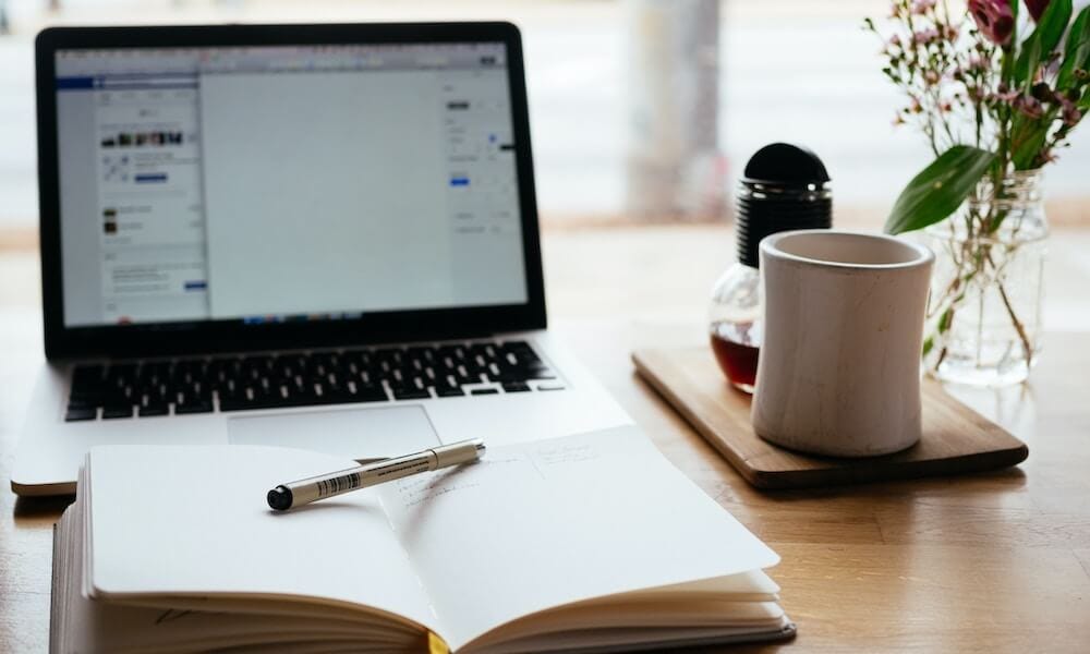 Desk with laptop, open notebook and mug