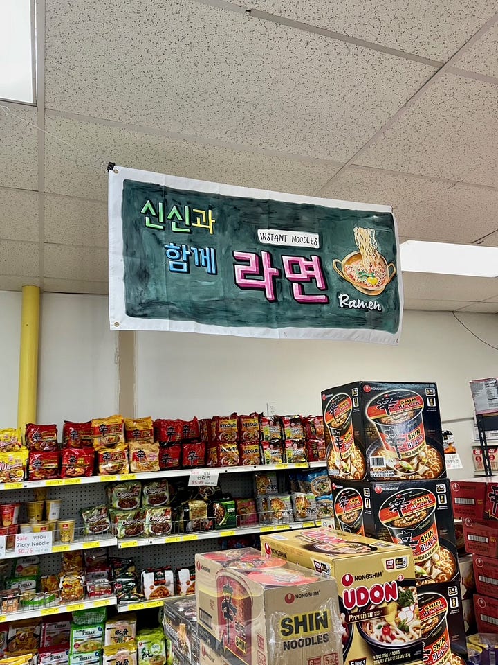 can of lee kum king chicken bouillon powder, full hand cart at korean grocery store, pot of korean noodles and green vegetables, mushrooms and chicken, hand-painted ramen sign hangs above shelves of ramen