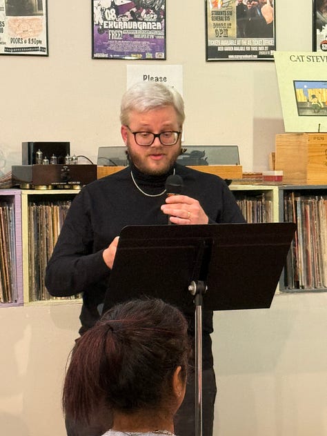 A group of people reading at an open mic inside a small wine bar.