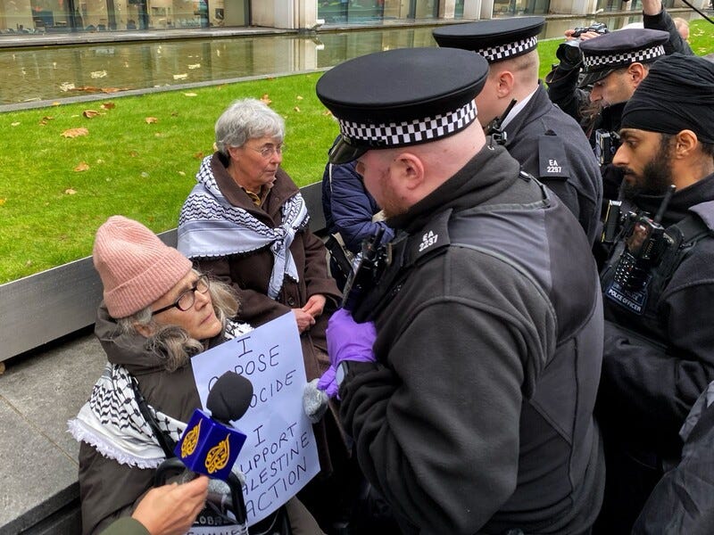 Police about to arrest two women holding signs saying they support Palestine Action Police about to arrest two women holding signs saying they support Palestine Action