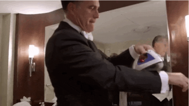gif image: In a hotel room, Mitt Romney uses a hot iron to touch up the sleeve of a suit jacket that he's already wearing. Steam rises from the iron and Romney's arm.