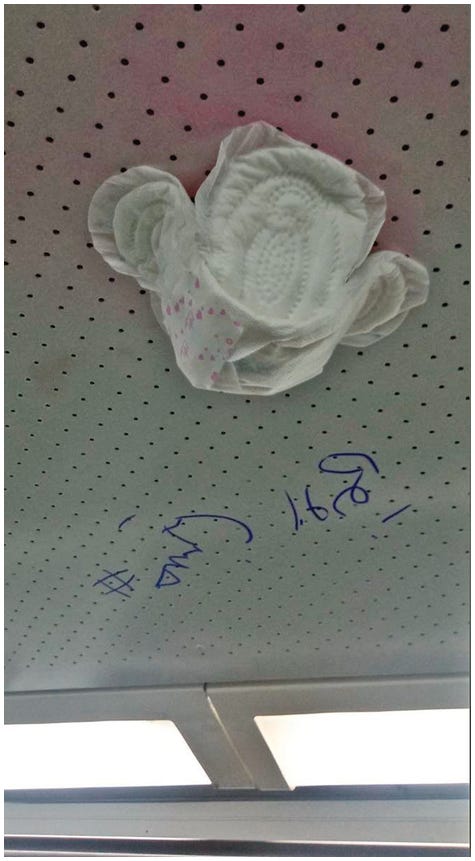 A grayscale photo features a sanitary pad stuck to a perforated ceiling panel with text in a foreign language written nearby.