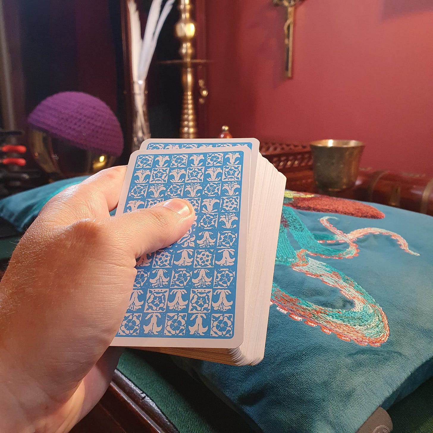 Hand holding a blue-backed tarot deck on embroidered fabric during the Callie Kazumi Tarot DMs interview.