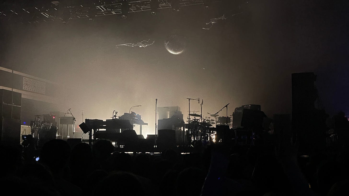 A stage covered in musical instruments, dramatically backlit so that everything appears in silhouette. This is the moment right before LCD Soundsystem takes the stage.