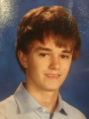 A boy with brown hair and eyes facing the camera against a blue background