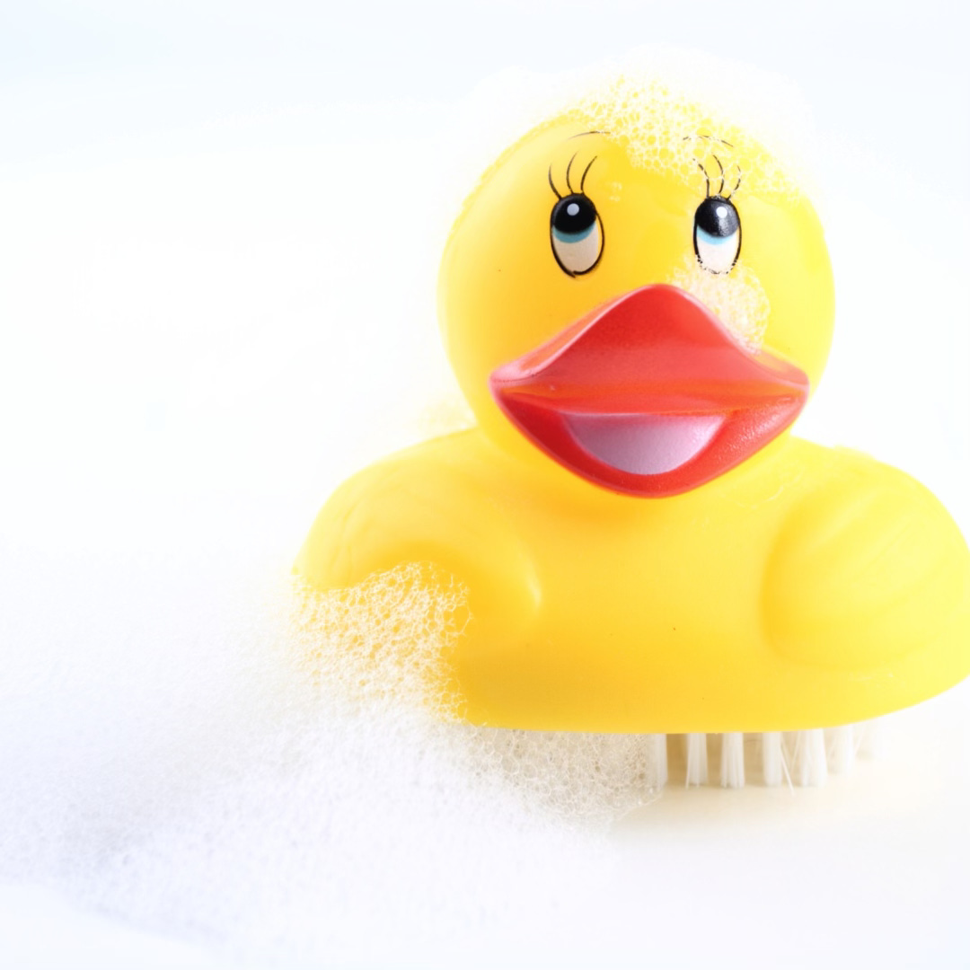 Photo of a duck hand-brush with soap suds on it. The duck is yellow and making a smiley face.