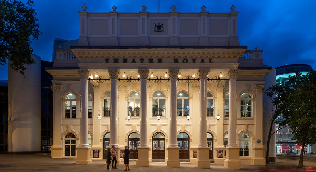 The Theatre Royal in Nottingham - an ornate cream building with arched windows - at night, with people standing in front of it
