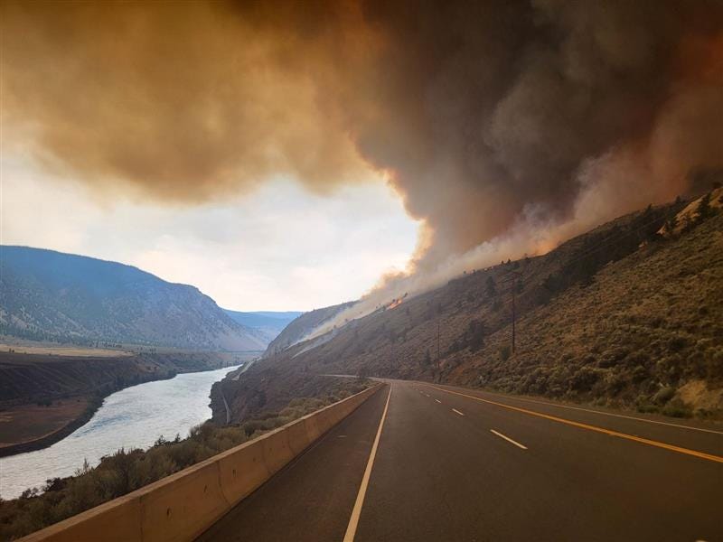 the shetland creek wildfire burning along a slope beside a highway with dark smoke rising in the air the shetland creek wildfire burning along a slope beside a highway with dark smoke rising in the air
