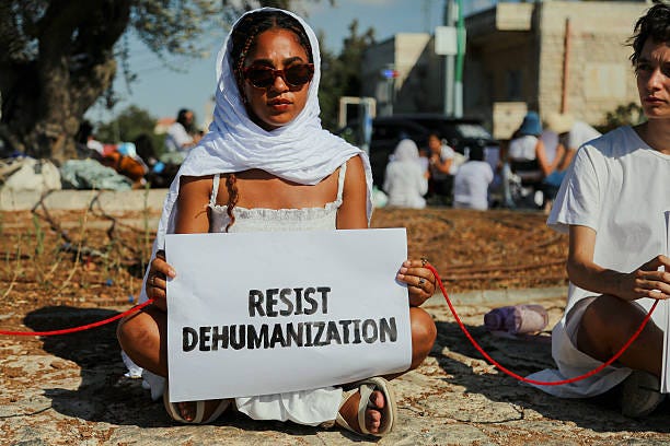 An activist holds a sign reading "Resist Dispossession" during a protest at the Beit Jala roundabout in Bethlehem District, West Bank, on August 29,...