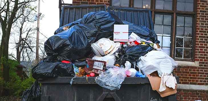 Photo of household waste overflowing from a large waste bin.
