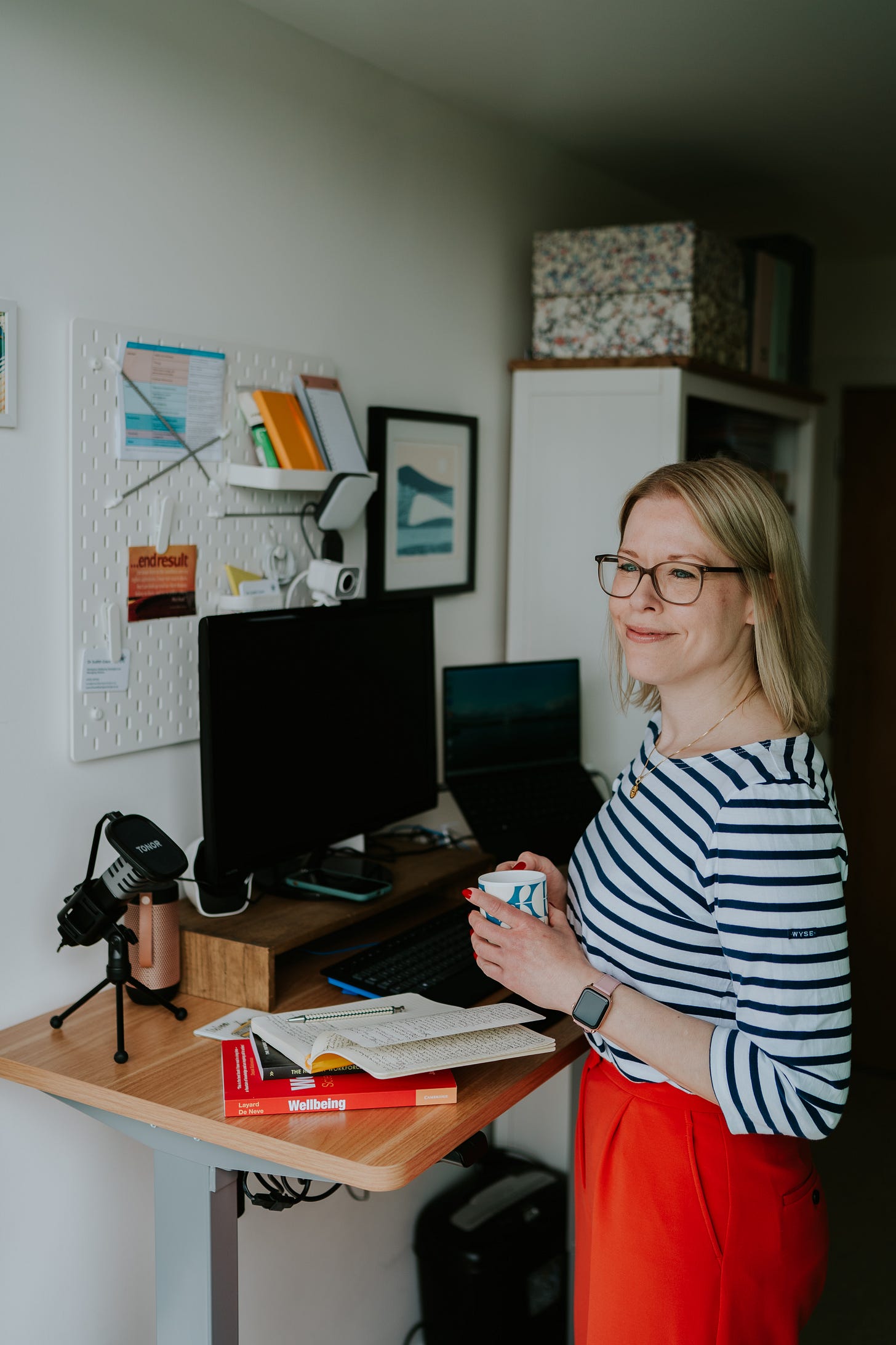 A woman stands next to her sit/stand desk with a coffee working from home.