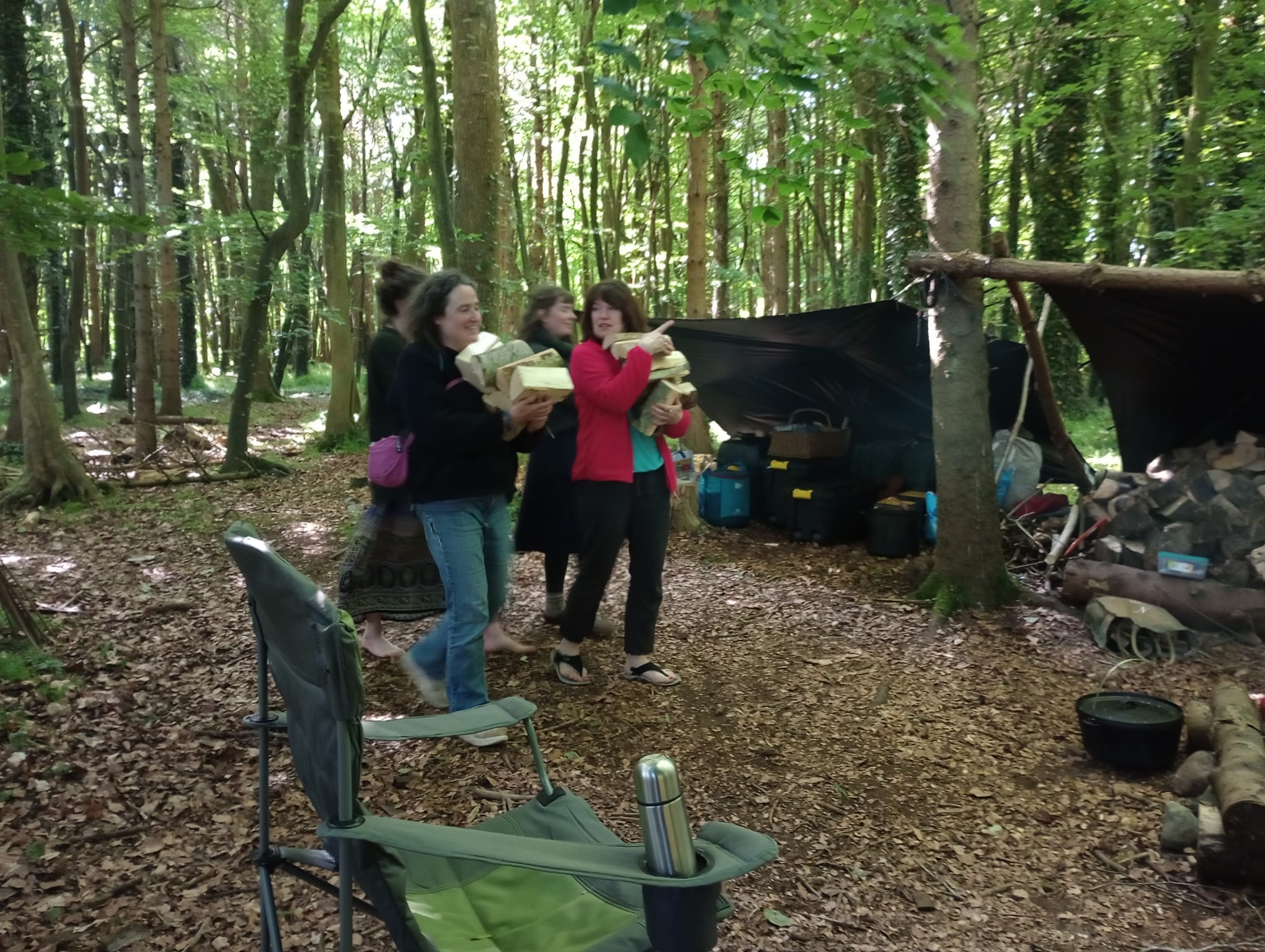 Four women weaving through the trees carrying logs for the wood pile. I'm on the right wearing a red fleece. We are all chatting.