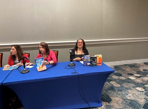 three images - first image of woman wearing red glasses, second image of table with black cloth, a woman signing a book and a woman standing in front of the table waiting for the book, third image is of a long table covered in blue cloth with two women seated and talking