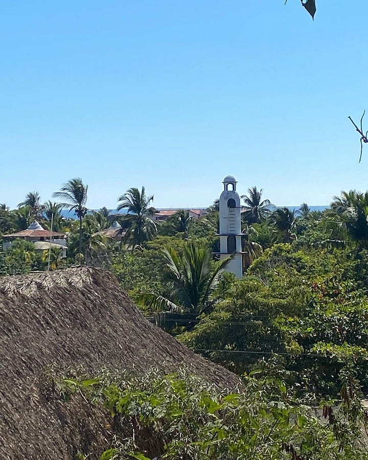 A multicolored rainbow staircase leads to restaurants on the main promenade of Zipolite. Palm trees and a white washed bell tower brush the clear blue skies from the vista of Hotel Punta del Sol