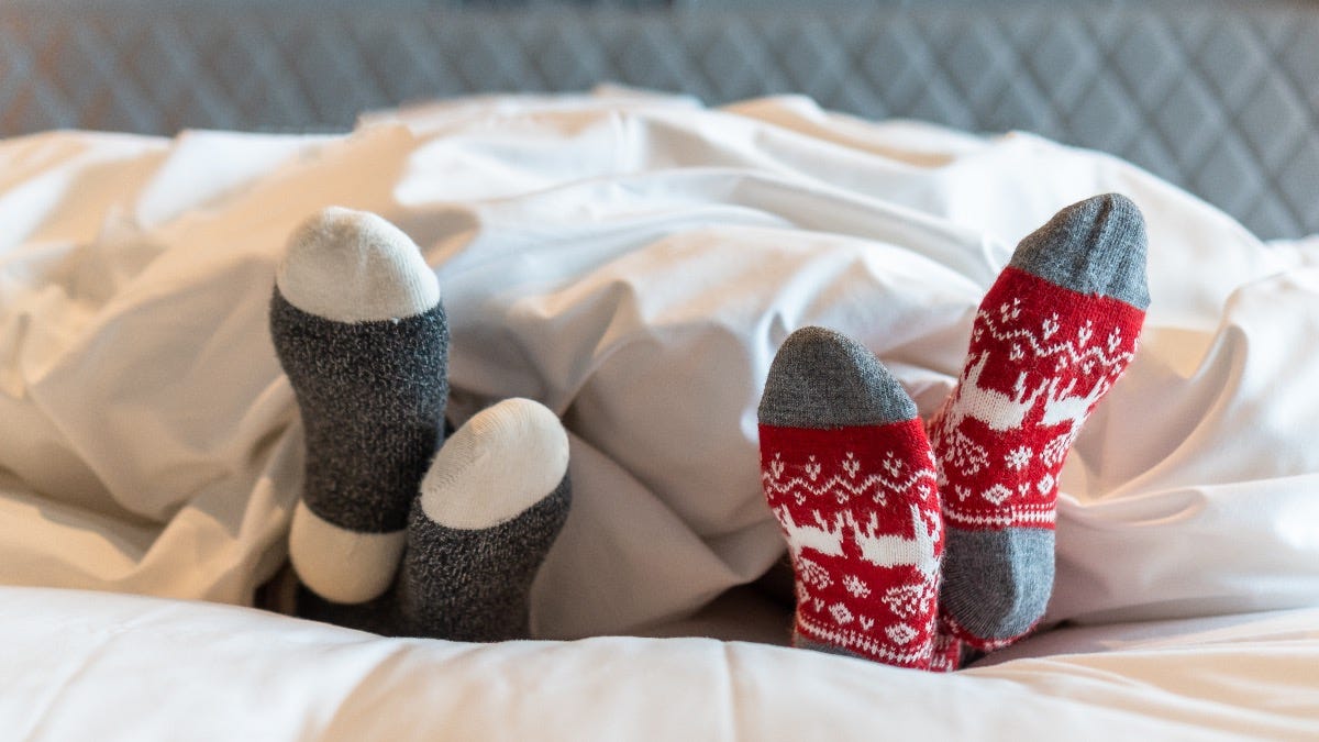 Couple’s feet in Christmas socks poking out from under the duvet Couple’s feet in Christmas socks poking out from under the duvet