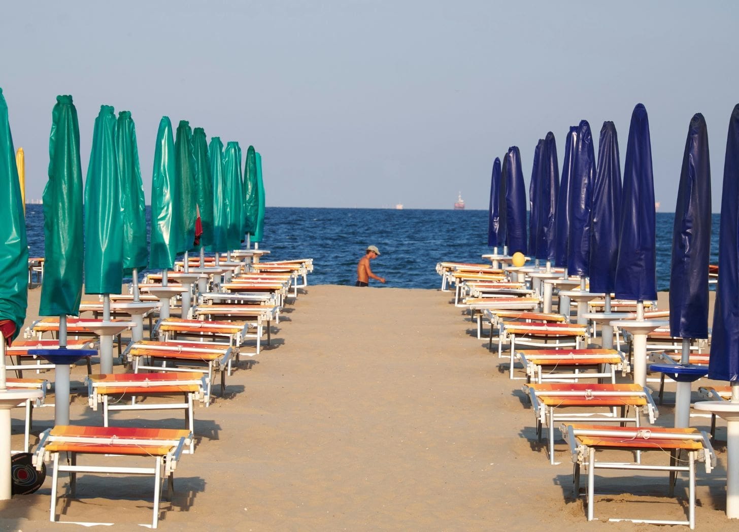 “A perfectly aligned row of blue and green umbrellas leading toward the sea, symbolizing balance, trust, and consistency in hospitality.