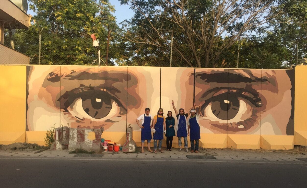 A group of people standing in front of a wall with a mural

Description automatically generated with low confidence