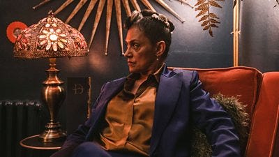 A woman sits in a decadent armchair looking suspicious of something off screen A woman sits in a decadent armchair looking suspicious of something off screen