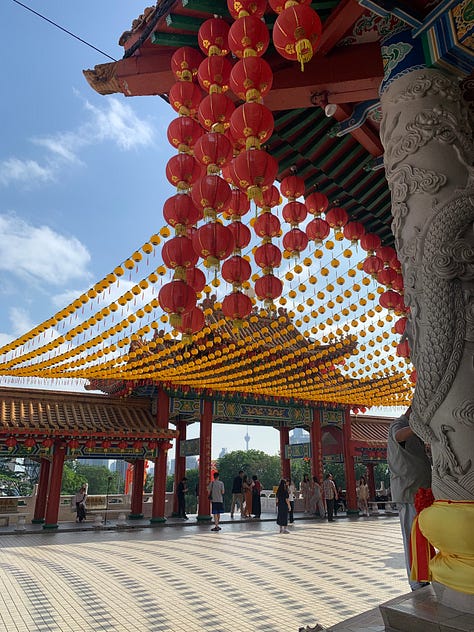 Two children aged 2 and 4 throw flowers into a fountain at a Chinese temple; red lanterns hang overhead at Thean Hou temple; a statue of an oxen in the garden at the temple.