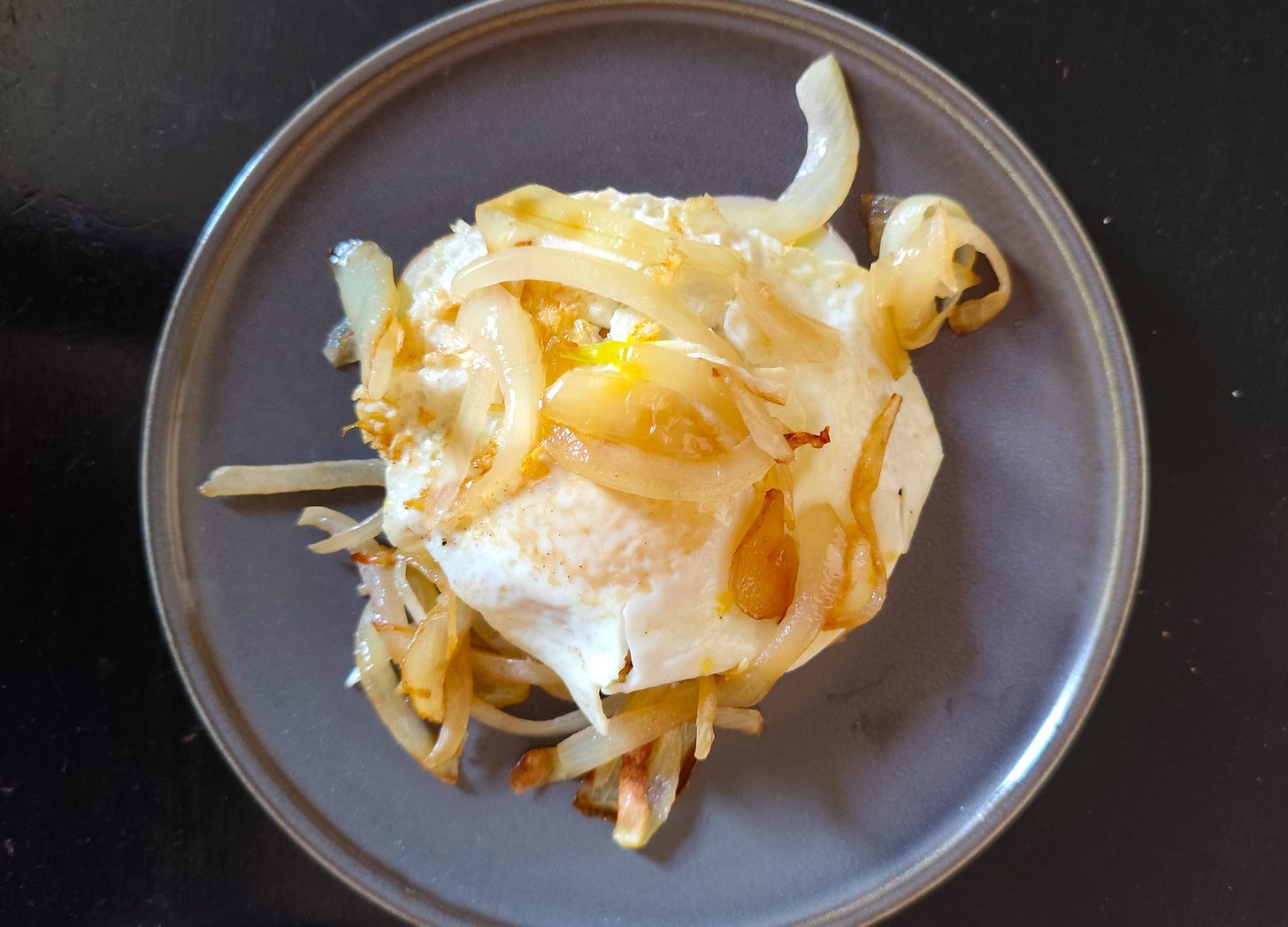 Fried egg with potatoes and golden caramelized onions on a gray plate, a perfect protein-packed breakfast or brunch. Find easy, healthy recipes, exclusive meal plans and cooking tips at AthleteMealPrep.com