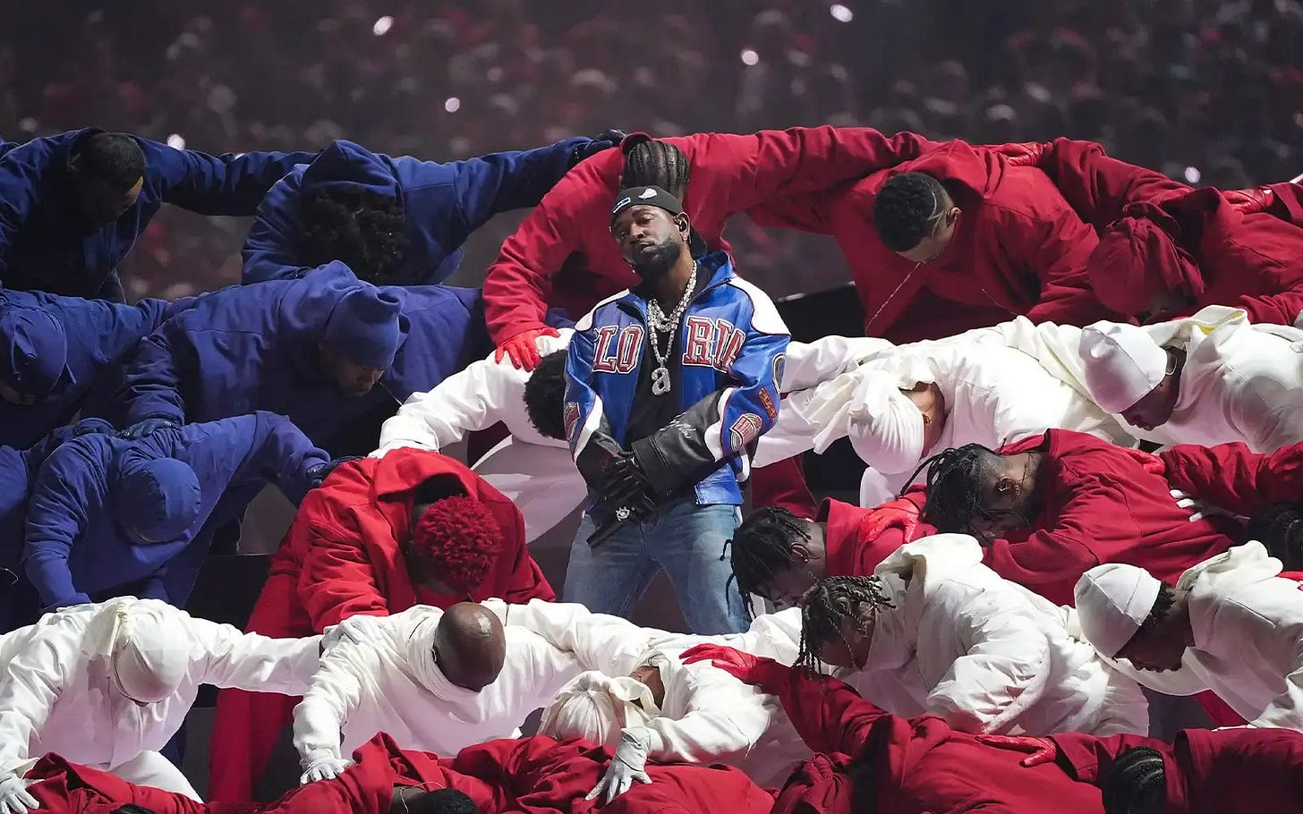 Kendrick Lamar standing in the middle of his performers who are wearing red, white, and blue and shaped in the American flag