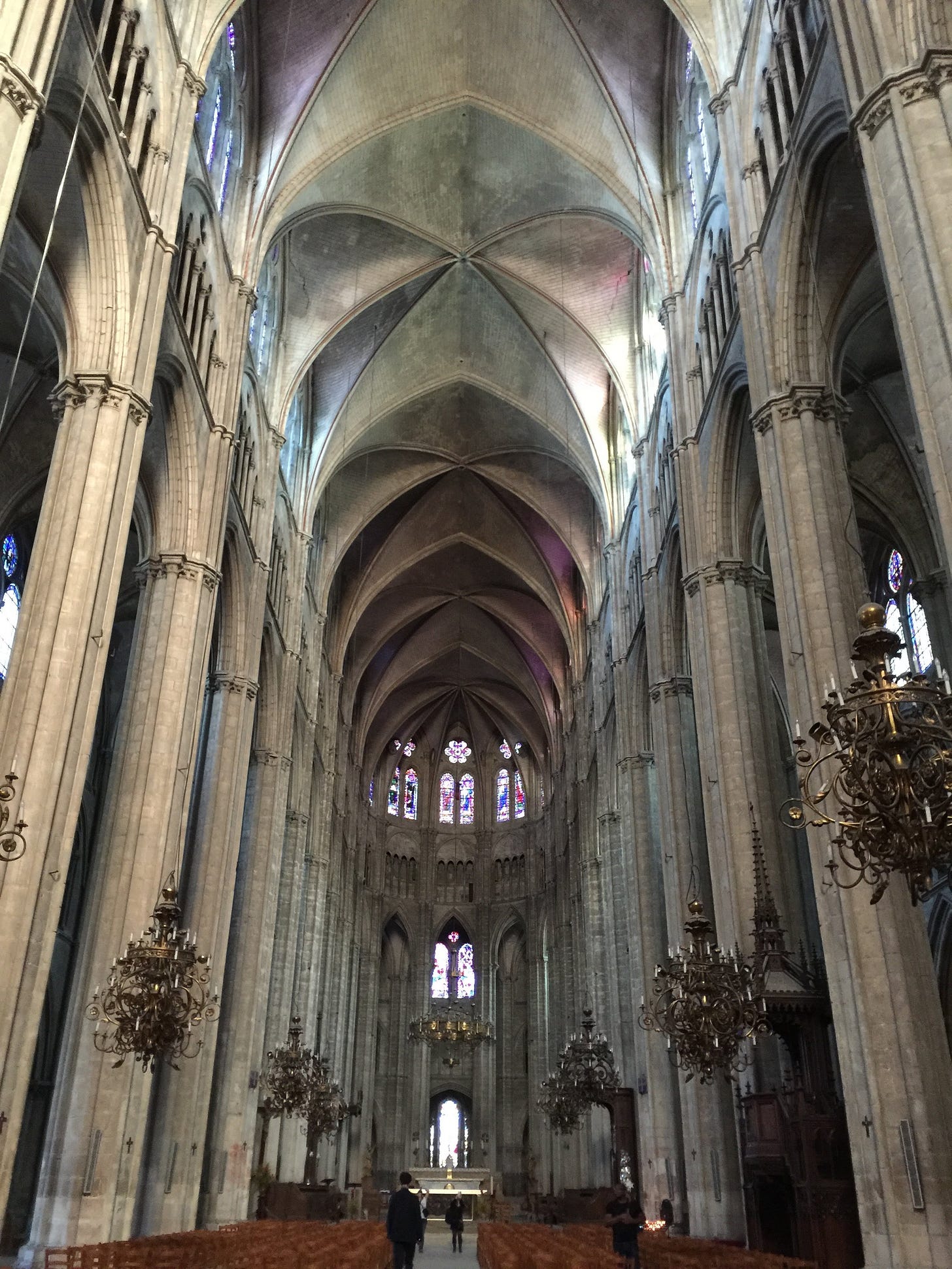 Interior of Bourges Cathedral in France, with soaring Gothic arches, tall stone columns, and stained-glass windows illuminating the nave.