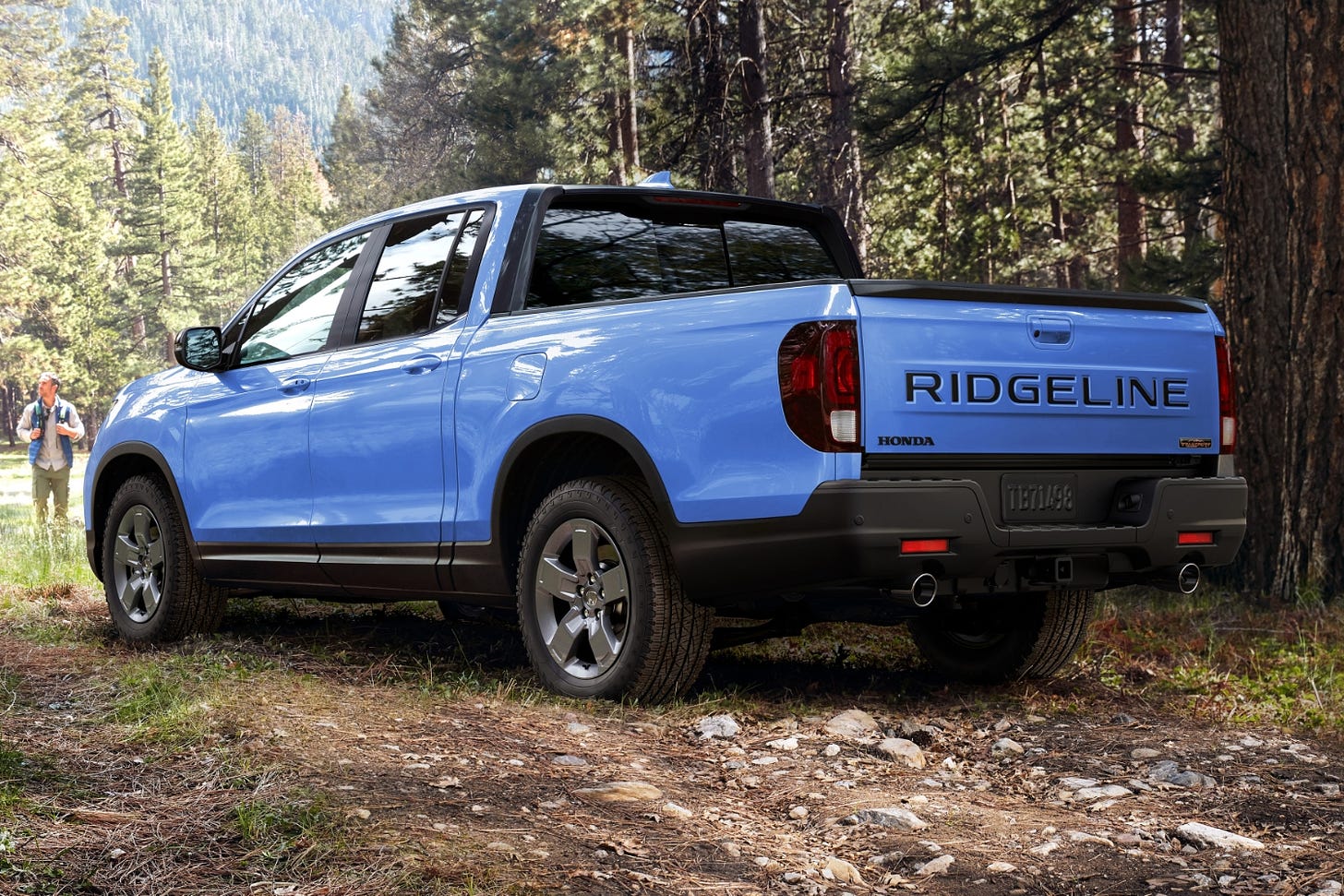 Rear quarter view of a blue 2024 Honda Ridgeline Trailsport parked in the woods.