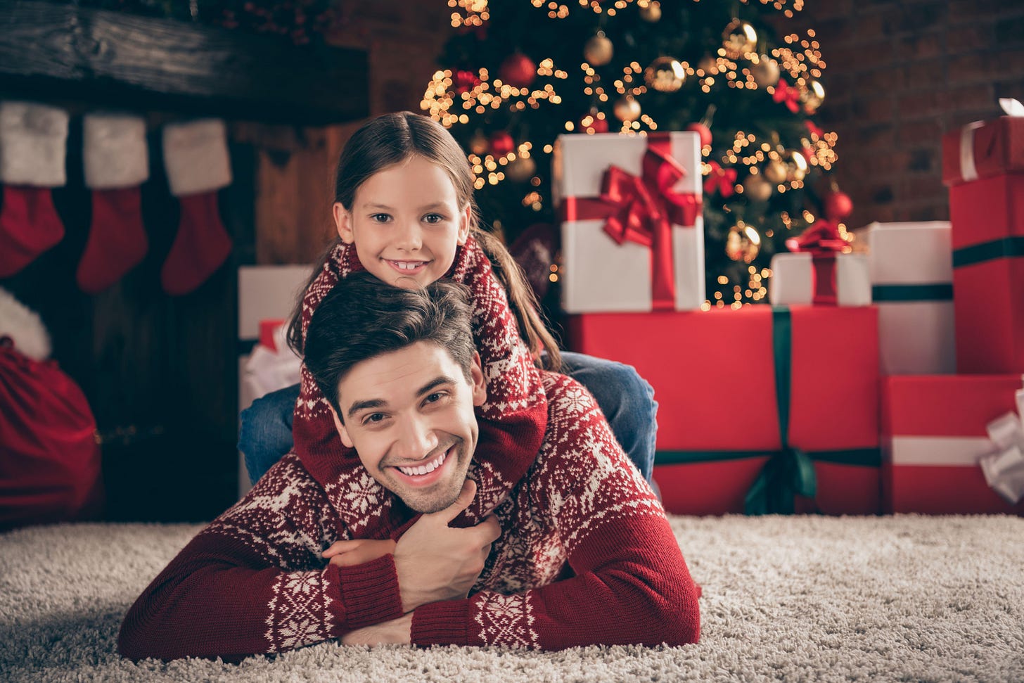 Single dad and daughter in matching christmas jumpers, sitting in front of christmas tree