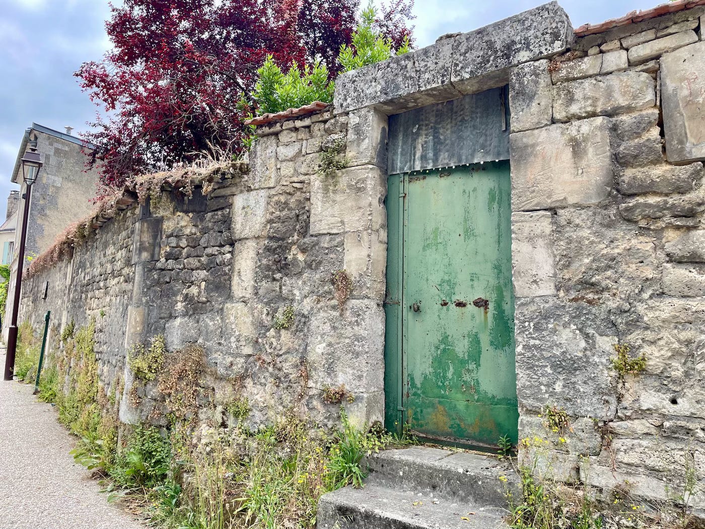 photo of an old green metal door in an old stone wall, Chateauneuf-Sur-Charente, France 2025