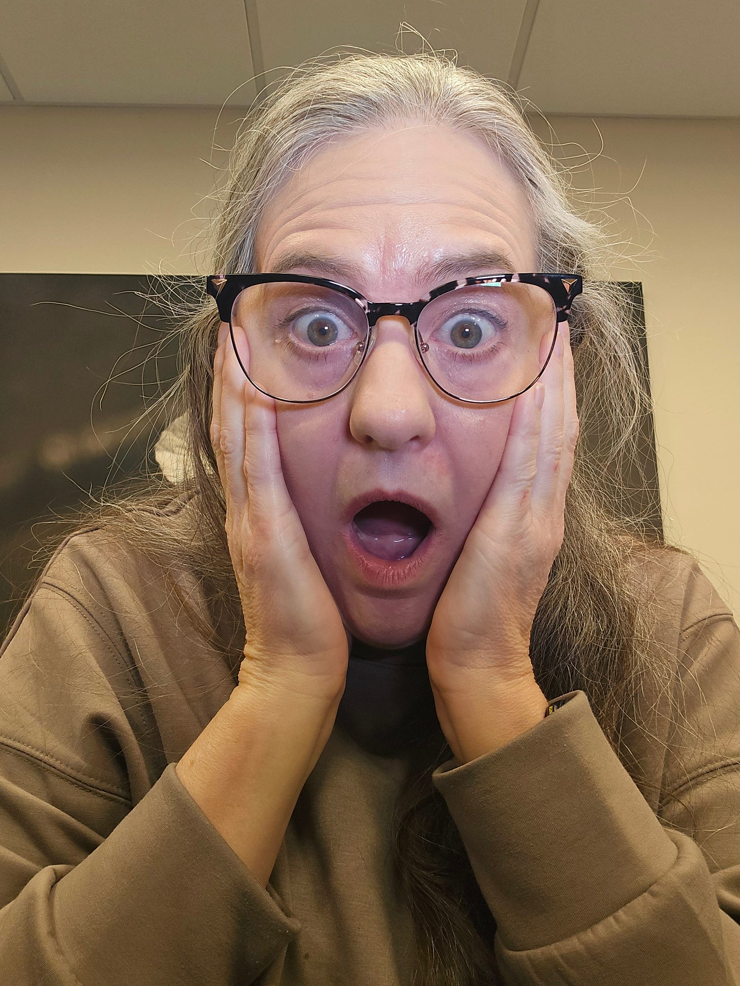 picture of author, glasses, long grey hair, eyes open in big surprise with hands on cheeks and open mouth of surprise