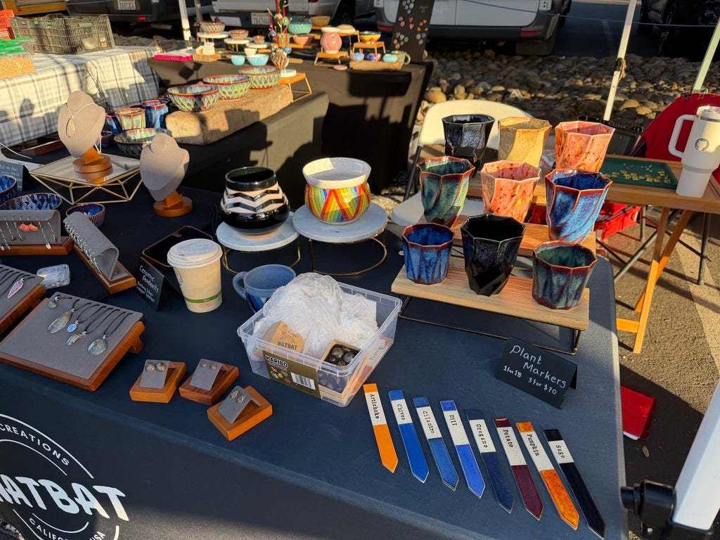 Outdoor craft market booth displaying handmade ceramics and jewelry on a navy tablecloth with 