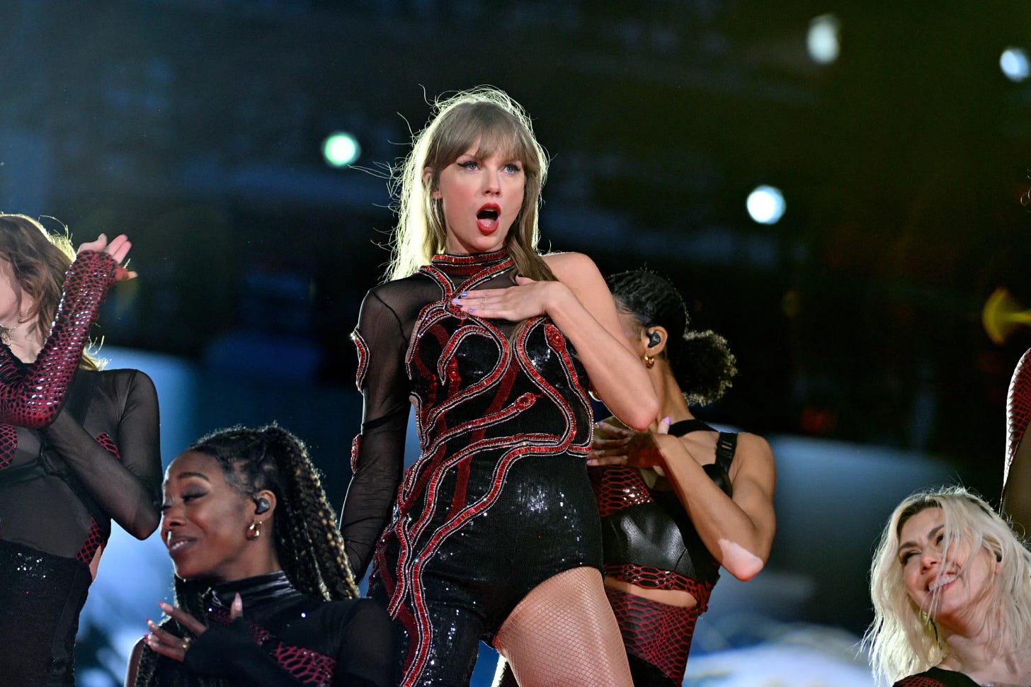 Taylor Swift in concert in a black dress, hand on her chest, looking empowered