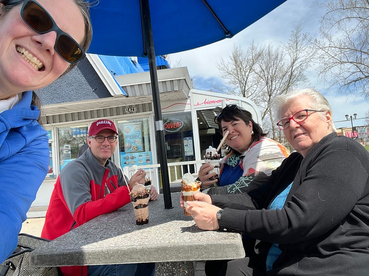 Four adults enjoying an ice cream at a picnic table on a sunny day.