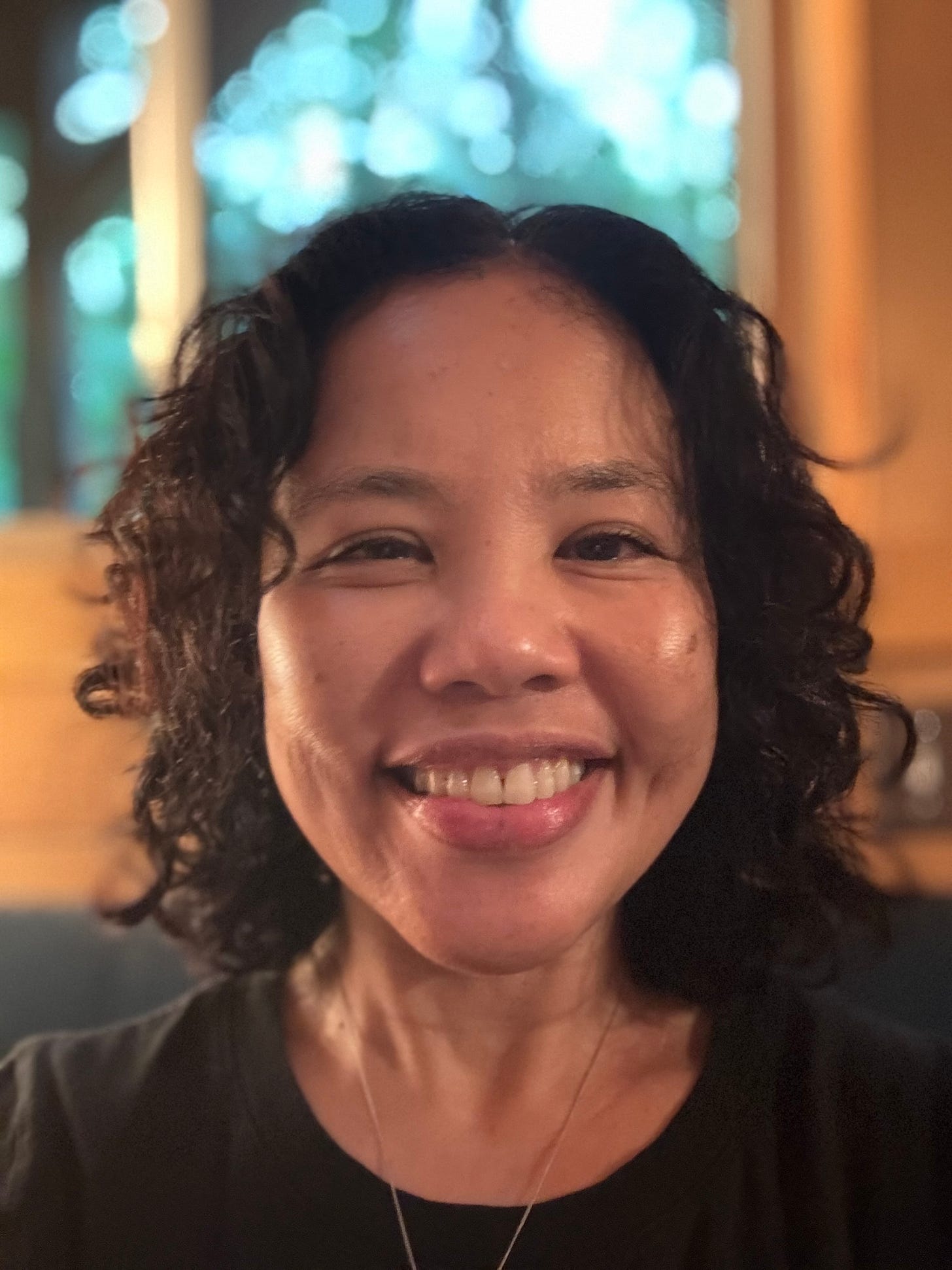 Photo of Barb Natividad, a Filipino-American woman with curly shoulder-length brown hair and a big smile