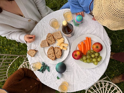 An overhead garden table with bread, cheese, carrots, apples, grapes and drinks; two children eating at a white bistro table with the château behind; two children running down a path toward the château.