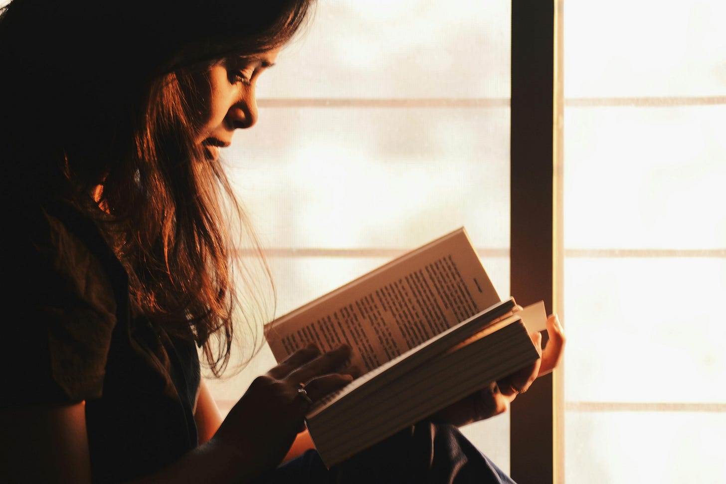 Woman reading a book beside the window Woman reading a book beside the window