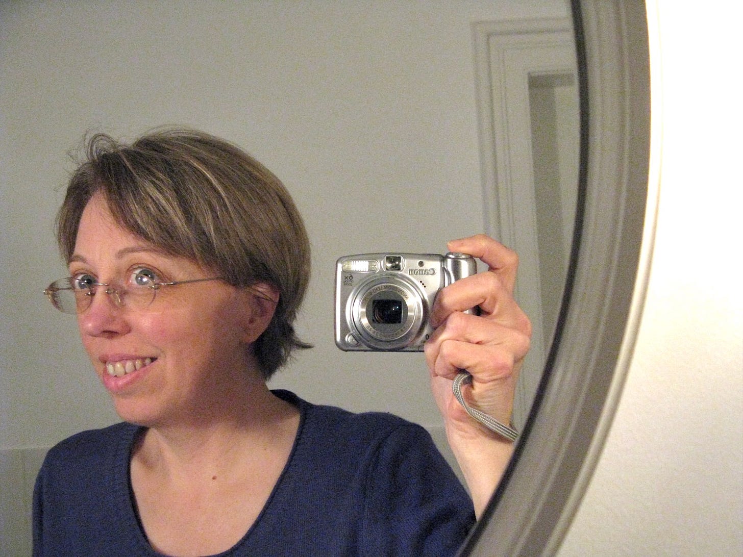 Woman in 40s smiling into curved mirror holding camera for self-portrait