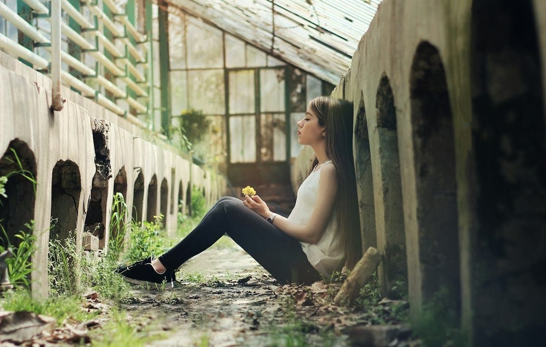 Girl sitting by wall holding flower