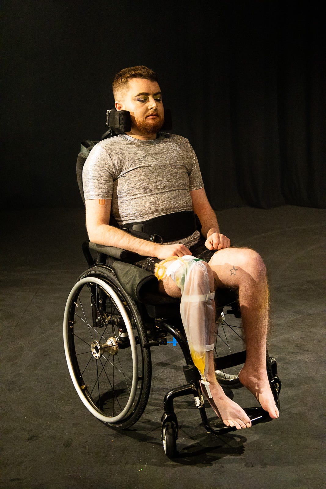 Jamie Hale, a white person is seated in a manual wheelchair, strapped in at the chest and legs, clearly immobile.